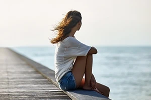 Junge Frau sitzt am Steg und schaut aufs Meer