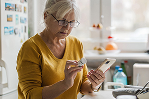 ältere Frau liest das Etikett ihres Medikaments und hält Smartphone in der Hand