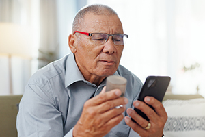 älterer Mann hält Medikament und Smartphone in der Hand