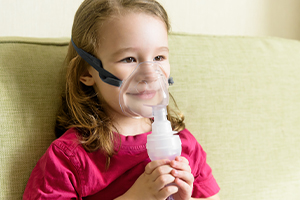 Little girl holds inhaler mask at home. Sick kid breathes through a nebulizer. Baby using equipment to treat asthma or bronchitis. Concept of treatment of children's respiratory and lung diseases.